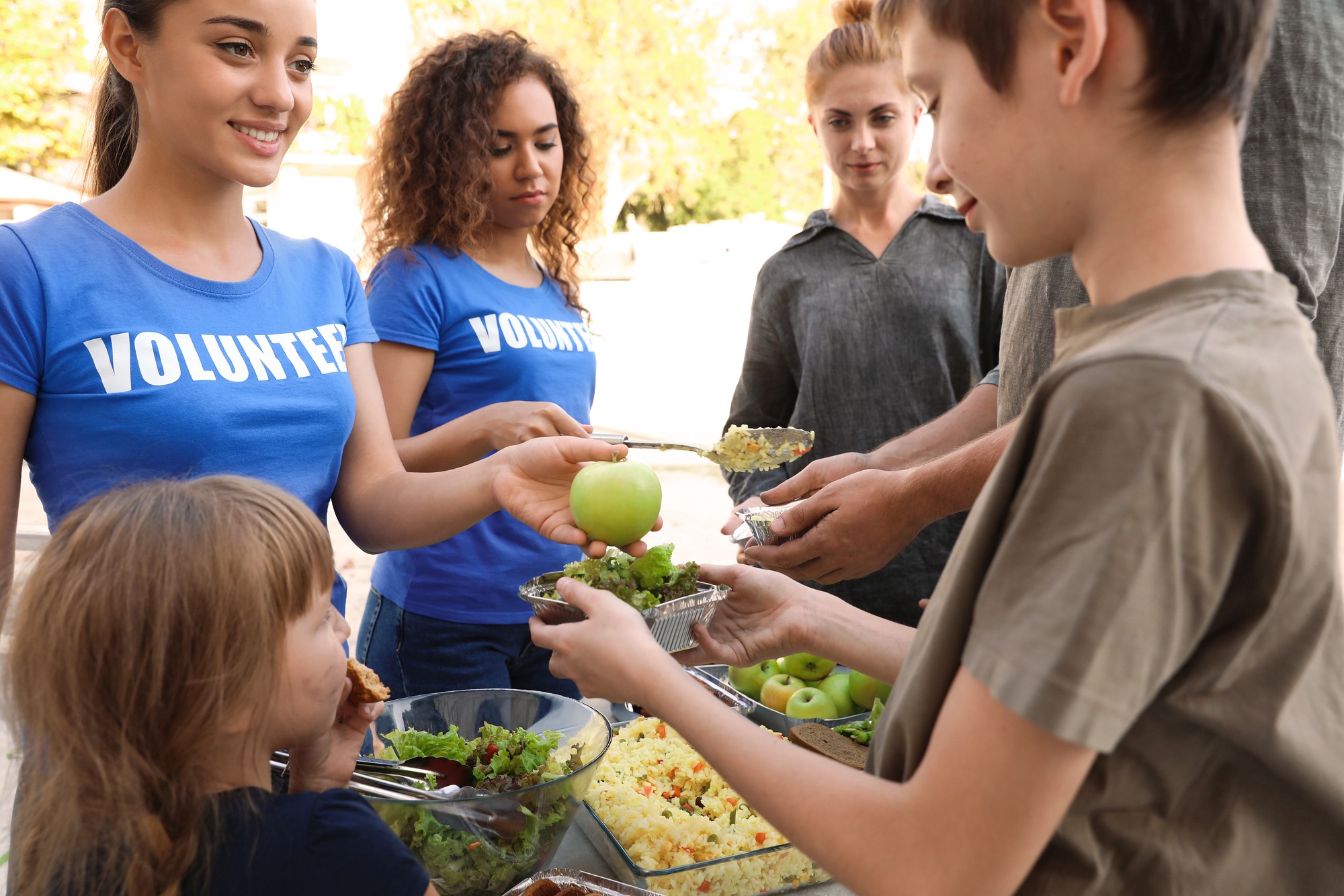 Volunteers serving food to poor people outdoors.